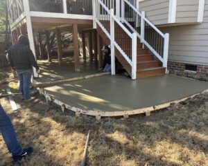 Workers pouring concrete under deck stairs.