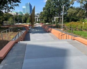 Modern walkway with tall sculpture and city buildings.