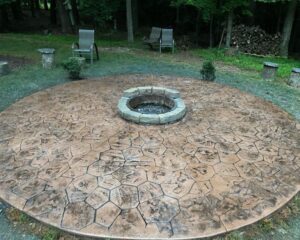 Stone fire pit on textured patio in backyard.