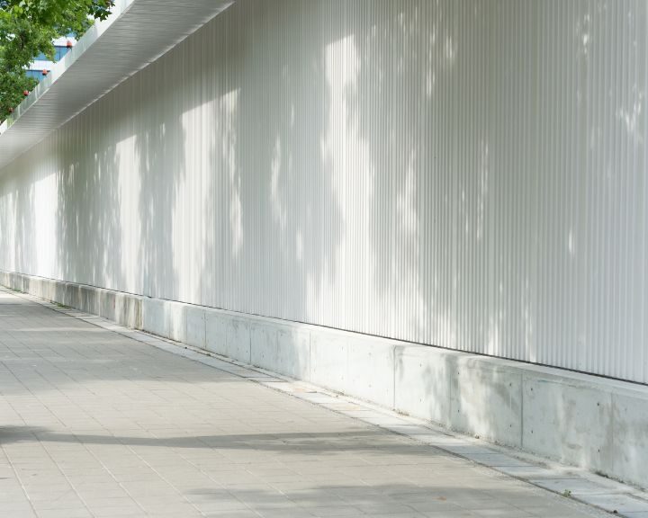 A sidewalk next to a white wall in the city.