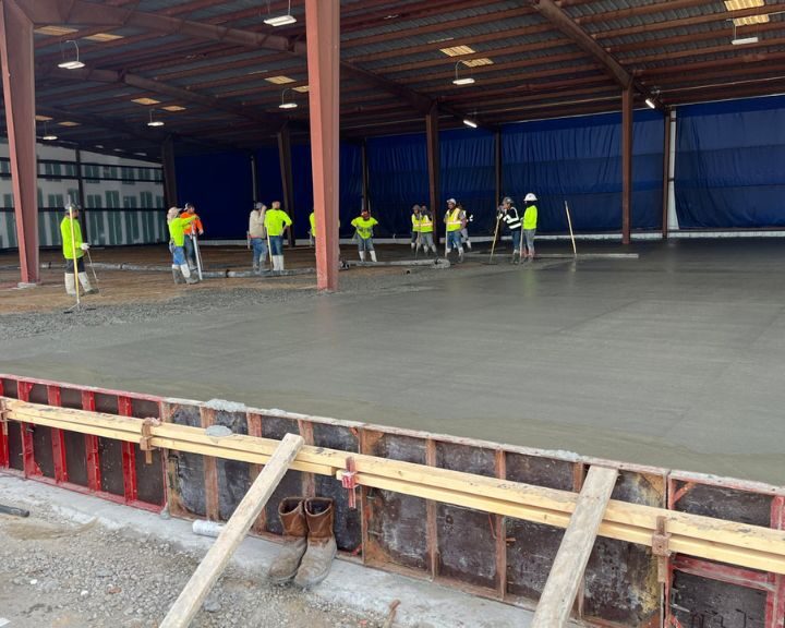 Workers smoothing freshly poured concrete in warehouse.