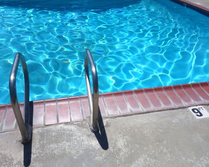 The blue pool with a concrete deck is located in the city.