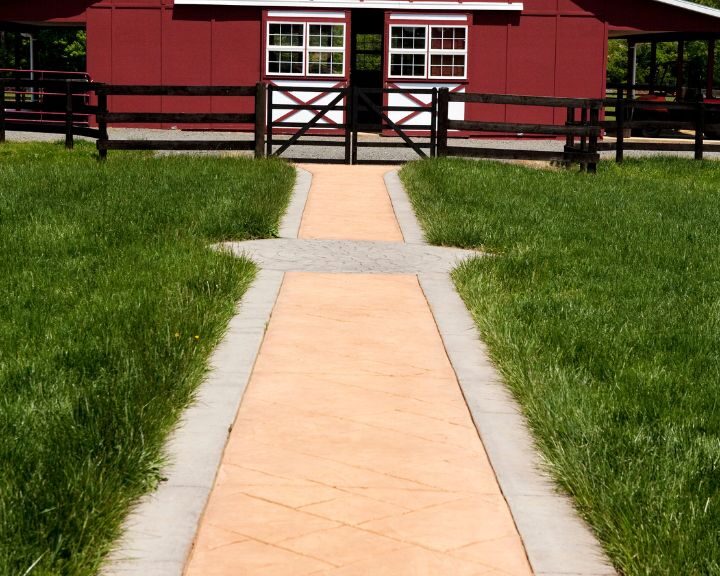 A city concrete pathway leading to a red barn.