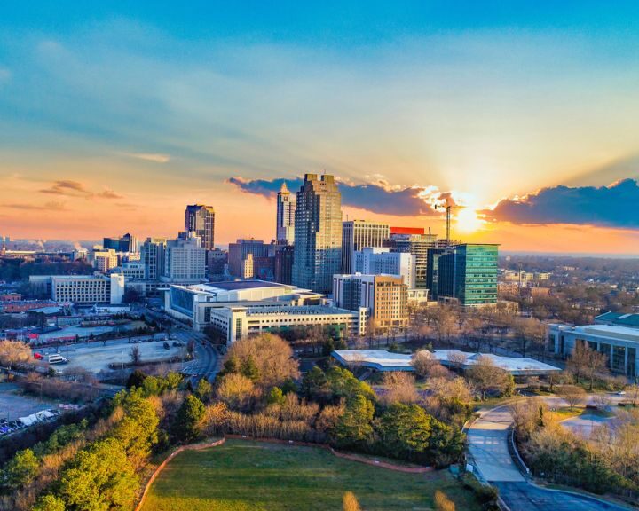 Sunset over city skyline with trees and buildings.
