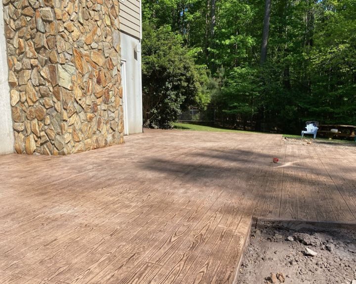 Spacious wooden deck next to stone wall.